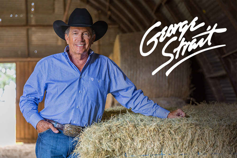 George Strait de pie en un granero junto a un fardo de heno.