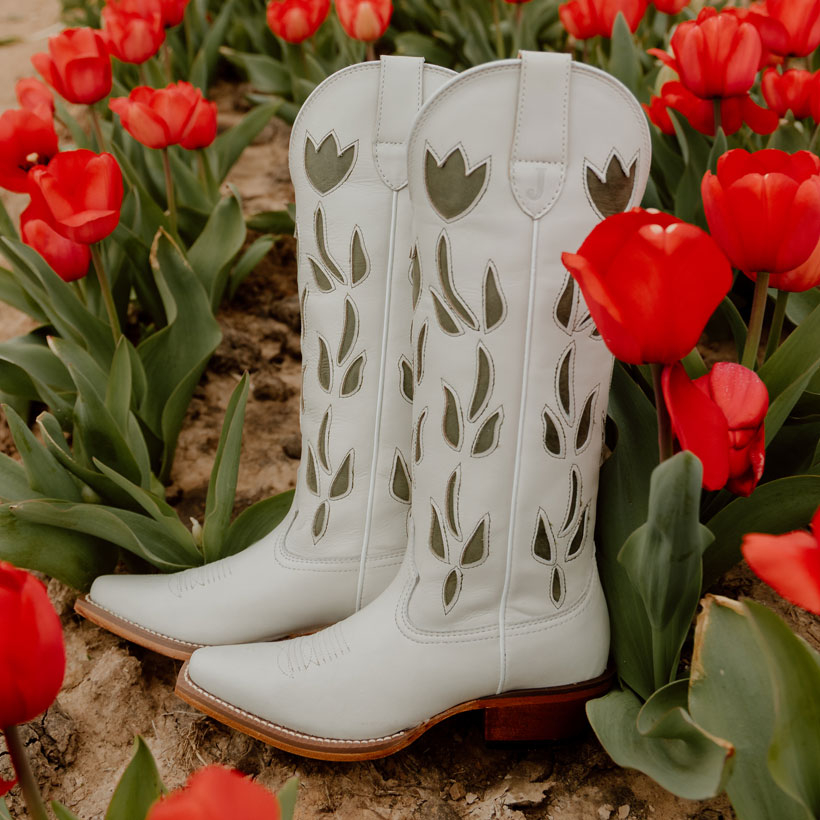The May 15" Western in Vintage White lying on a bed of red tulips.