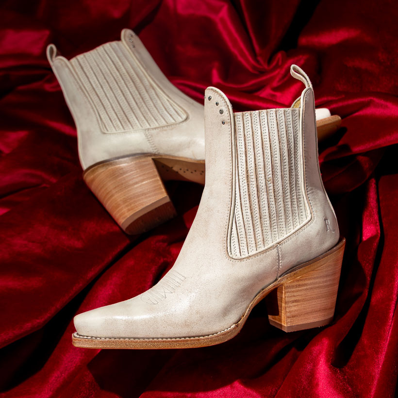 The Reba By Justin Hart 6" Western Bootie in vintage ivory (white) lying on a red velvet drapery.