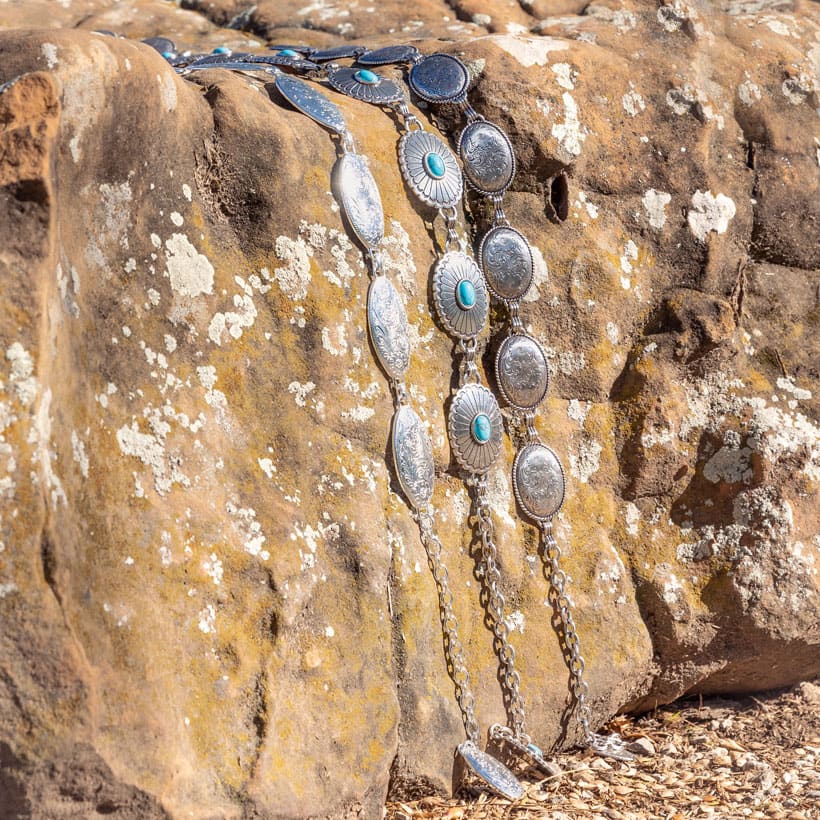 The Farmington Classic Chain Belt in silver, The Nicole Concho Link Belt in silver, and Concho Chain Belt in siver place on a rock.