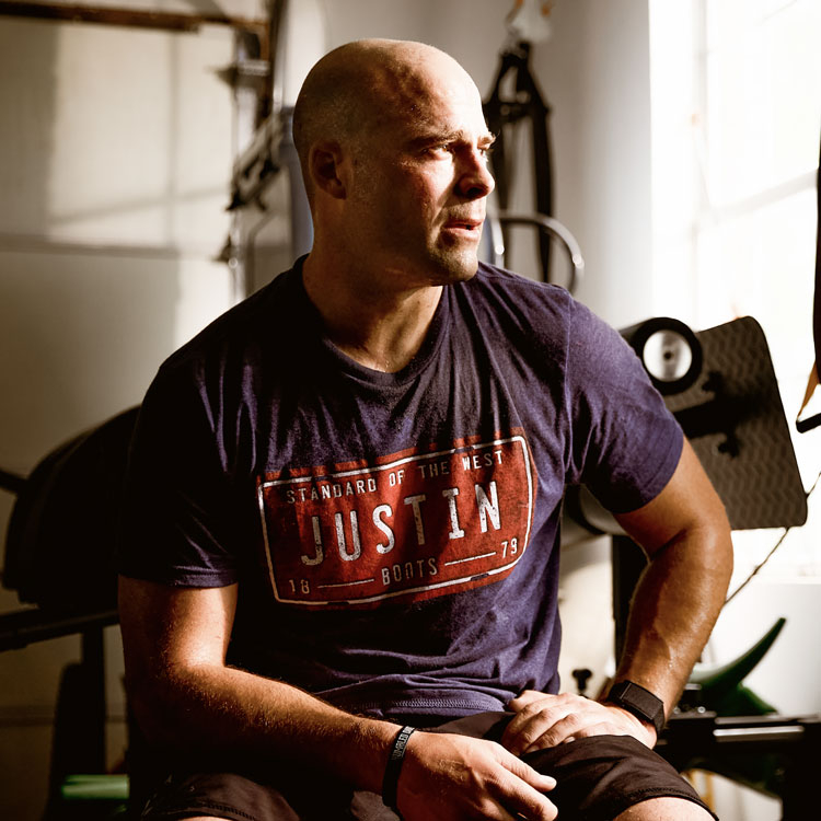 A man, Dusty Tuckness wearing a Justin T-shirt while sitting in a gym.
