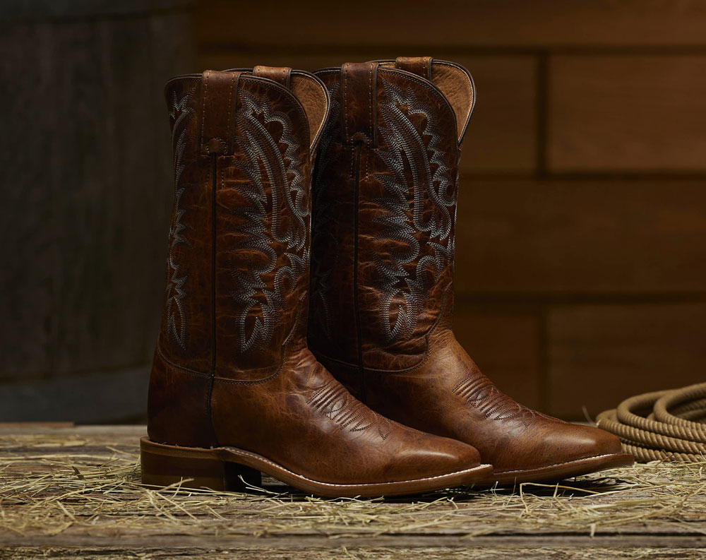 The Justin Peyton 11" Western Boot in Amber Brown on a barn floor.