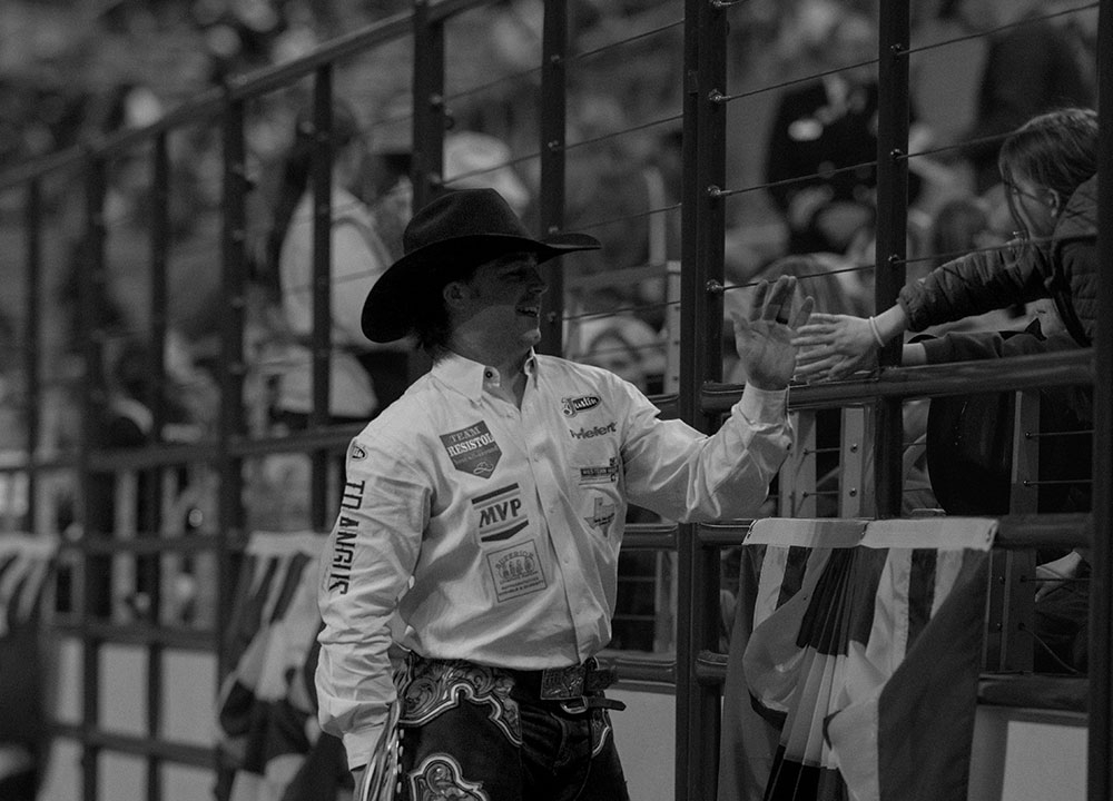 Wyatt Casper choca la mano con un joven aficionado desde la cerca de la arena en el Fort Worth Stock Show & Rodeo mientras lleva un sombrero vaquero y equipo de rodeo.