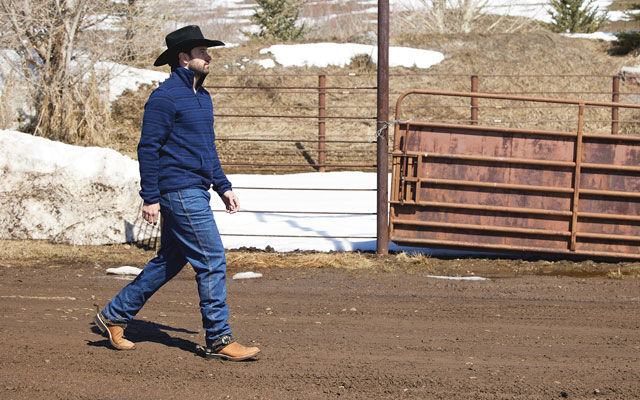 A cowboy walking in front of a fence wearing Justin Works boots.