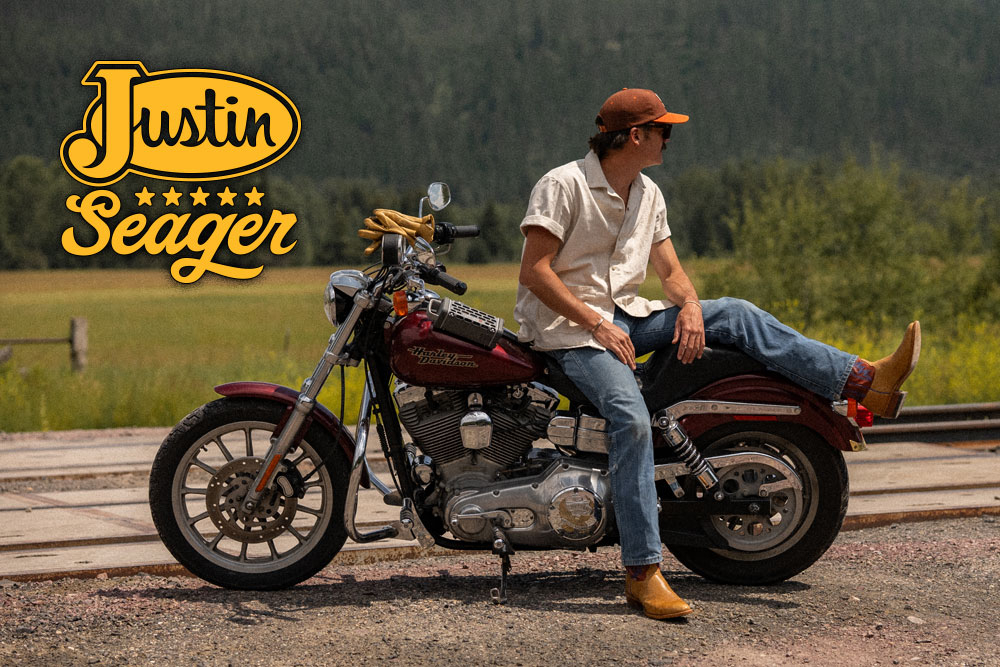 Justin by Seager. A man wearing The Stage Western Boots in desert tan sits on a motor cycle and looks off into the distance.