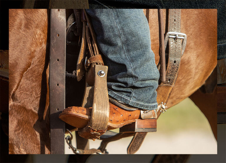 A close up photo of a man wearing Justin Exotic boots on a horse.