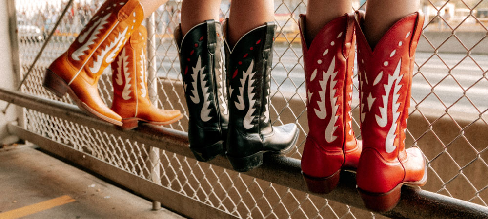 Mujeres que llevan las botas vaqueras Faye de 13 pulgadas en rojo, negro y color co&ntilde;ac (bronceado).