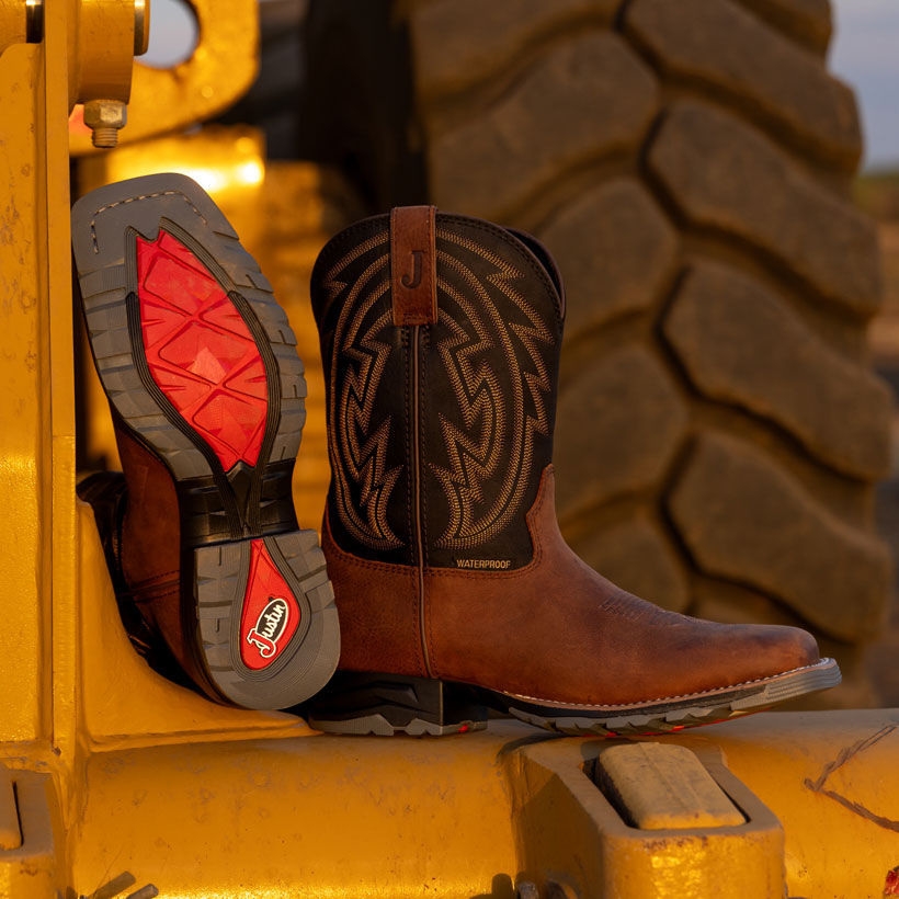 Bota de trabajo Lytle de 11 pulgadas, impermeable y con puntera de acero, en color marr&oacute;n/negro, sobre un tractor.