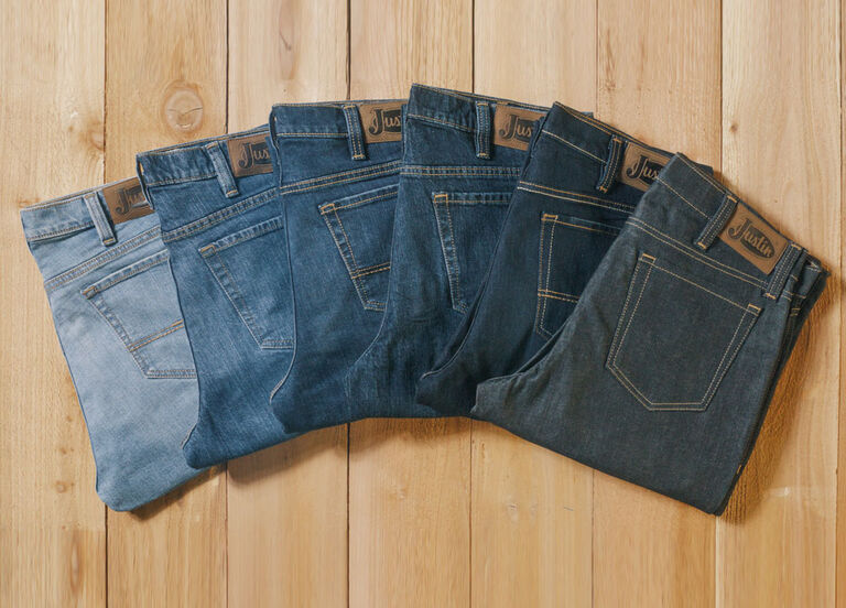 A wooden background lay down with different washes of Justin jeans folded and laying down on it.
