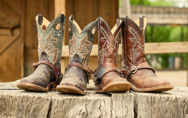 Two pairs of Bent Rail boots with spurs on posed on a log.