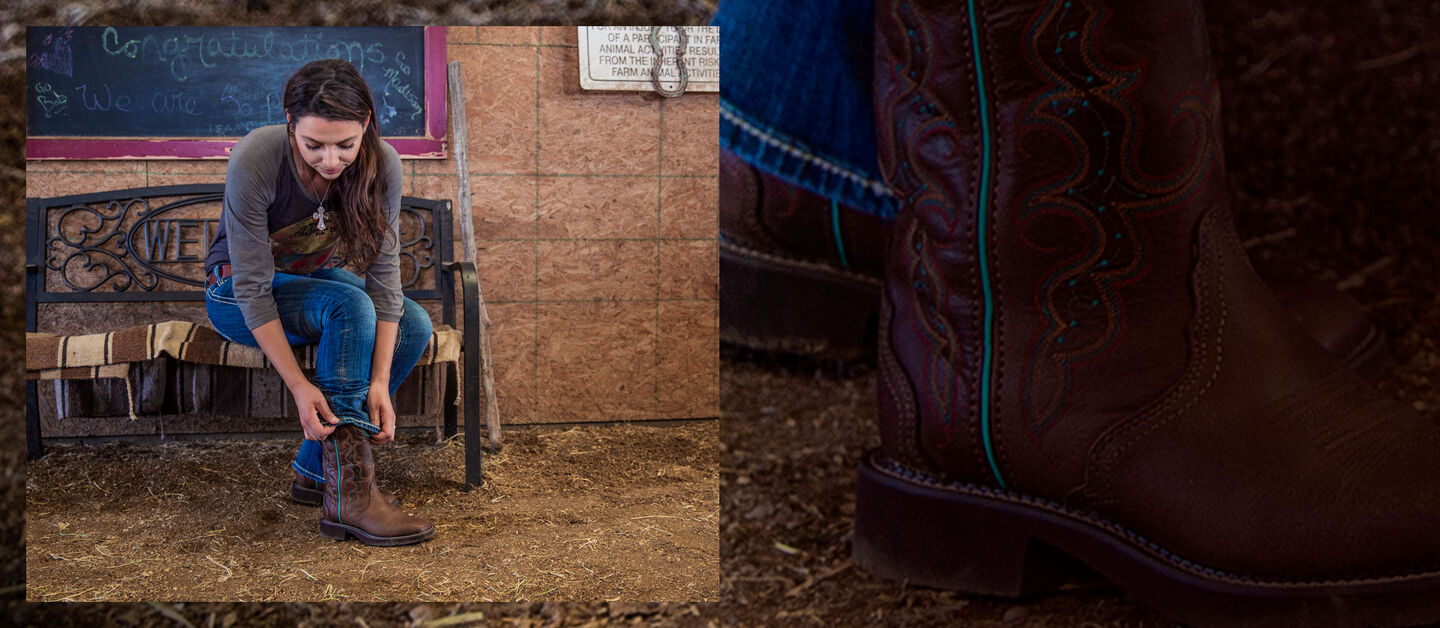 A woman sitting on a bench in a barn putting on Justin Gypsy boots.