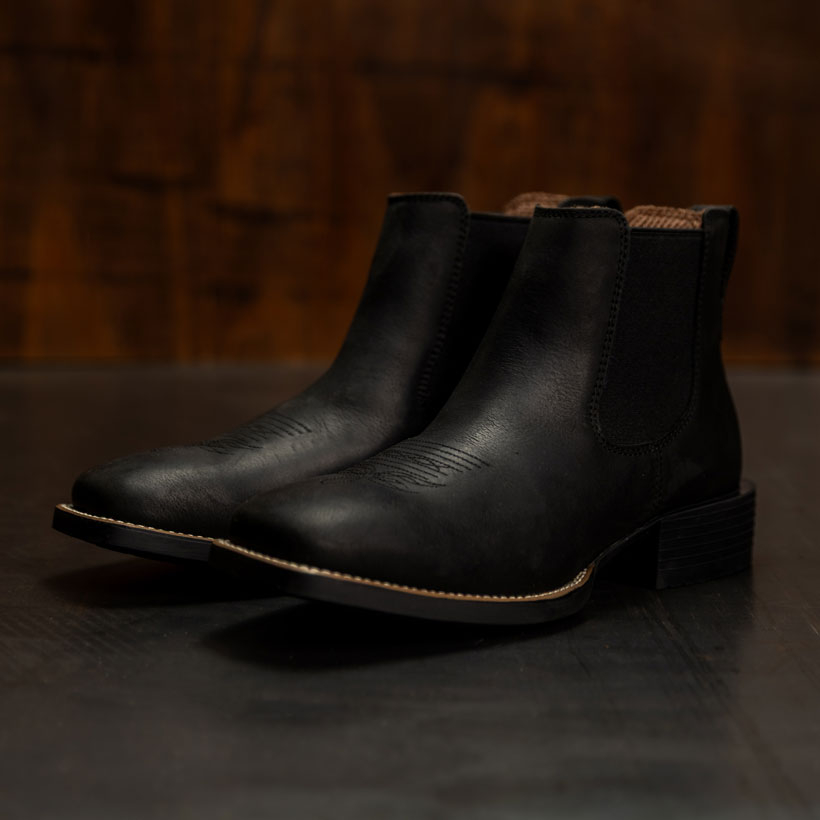 The Norman 6" Western chelsea boot in Black on a dark floor.