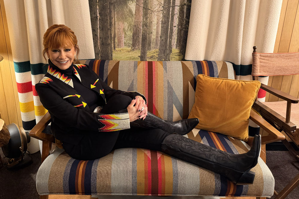 Reba McEntire smiling sitting on a couch wearing the Rumor 17" Western boots in black.