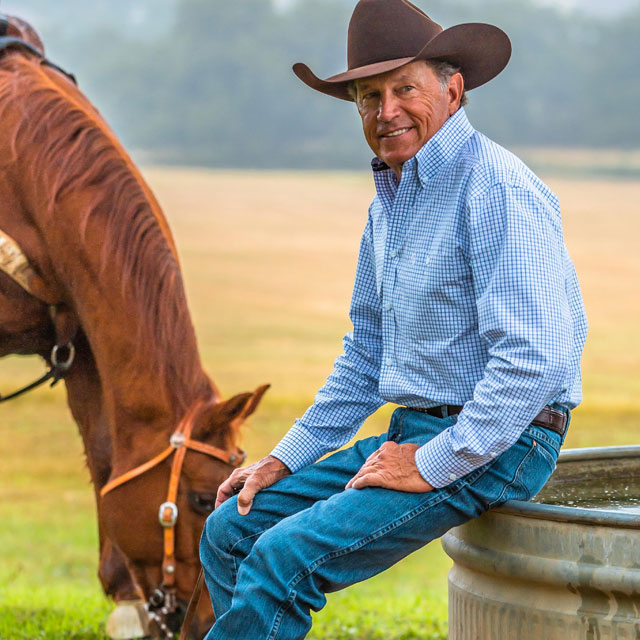 George Strait wearing a cowboy hat while sitting next to a horse.