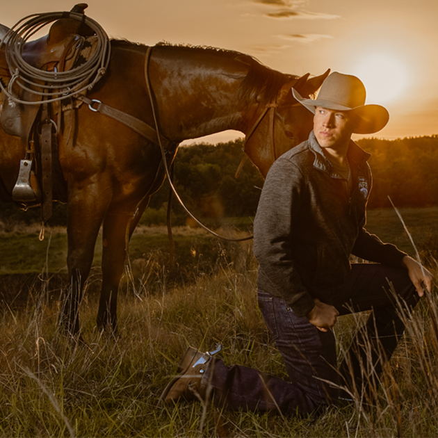 A man, Cody Webster kneeling next to a horse.