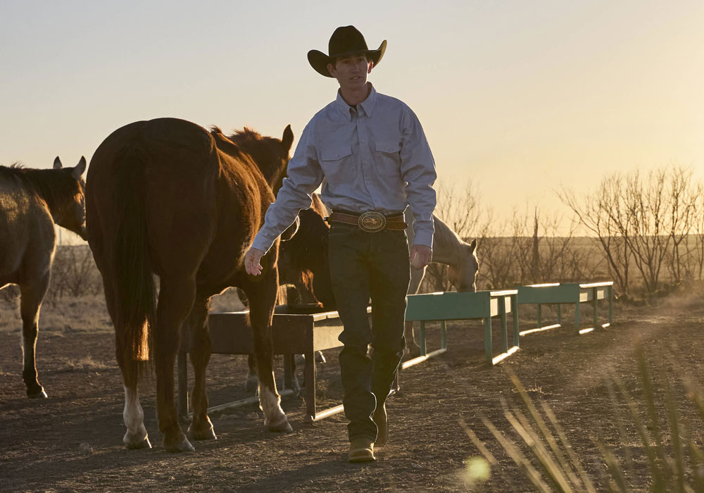 A man wearing The Justin Big News 11" Western Boots in Pecan Brown while working on a ranch.
