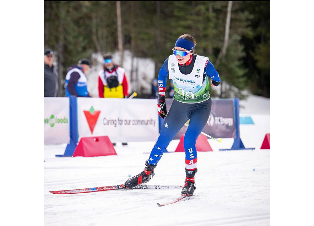 Para cross-country skier racing on a snowy course while wearing a USA team uniform, pushing forward on red Madshus skis during competition with spectators and race signage in the background.