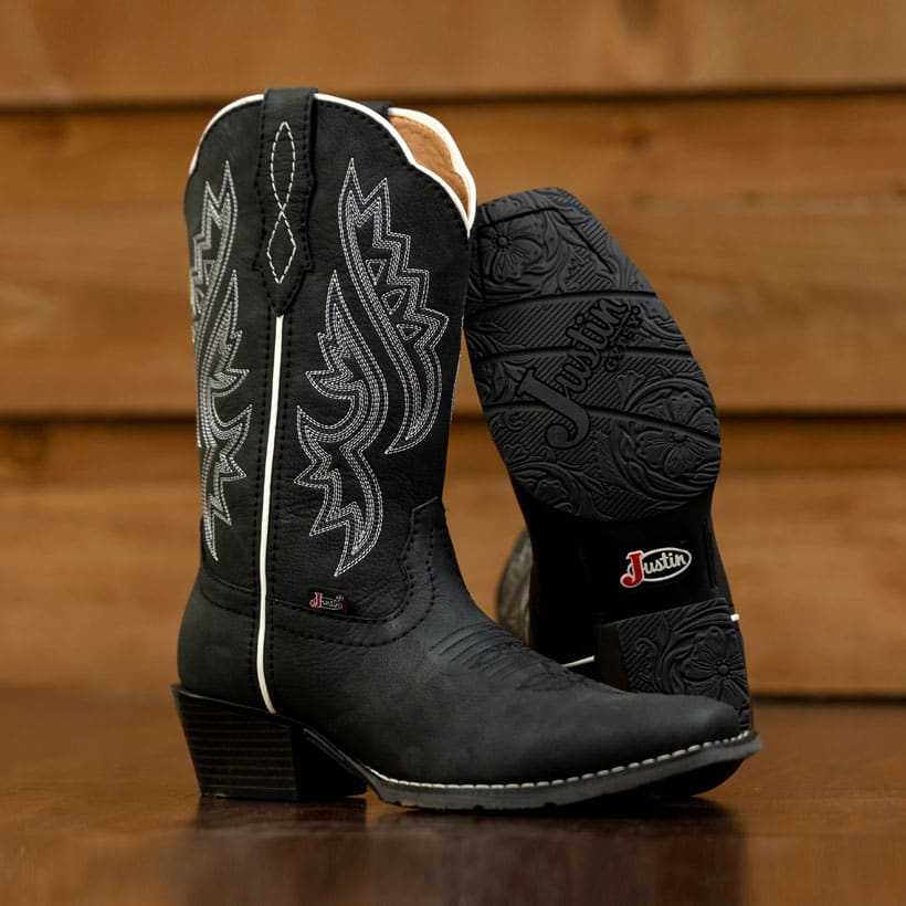 The Dezi 10" Western boot in Black on a wood floor.