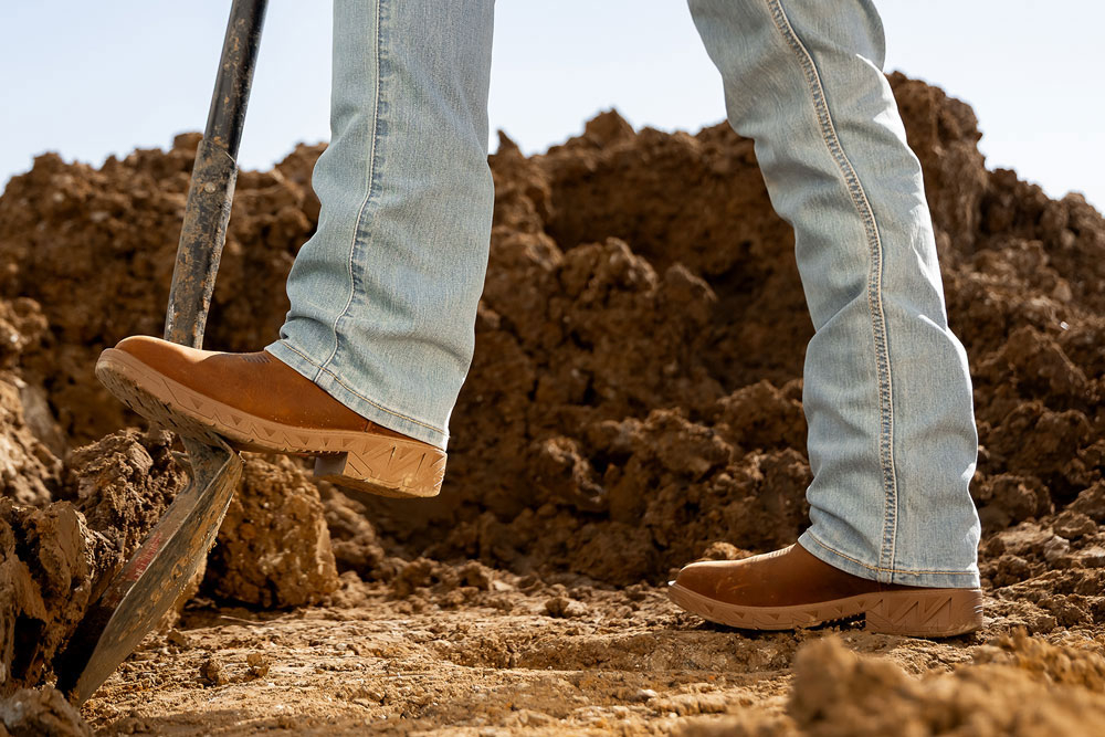 Un hombre usando la bota de trabajo Markout con punta de acero en color marr&oacute;n, con el pie apoyado sobre la parte superior de una pala.