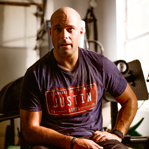 A man, Dusty Tuckness wearing a Justin T-shirt while sitting in a gym.