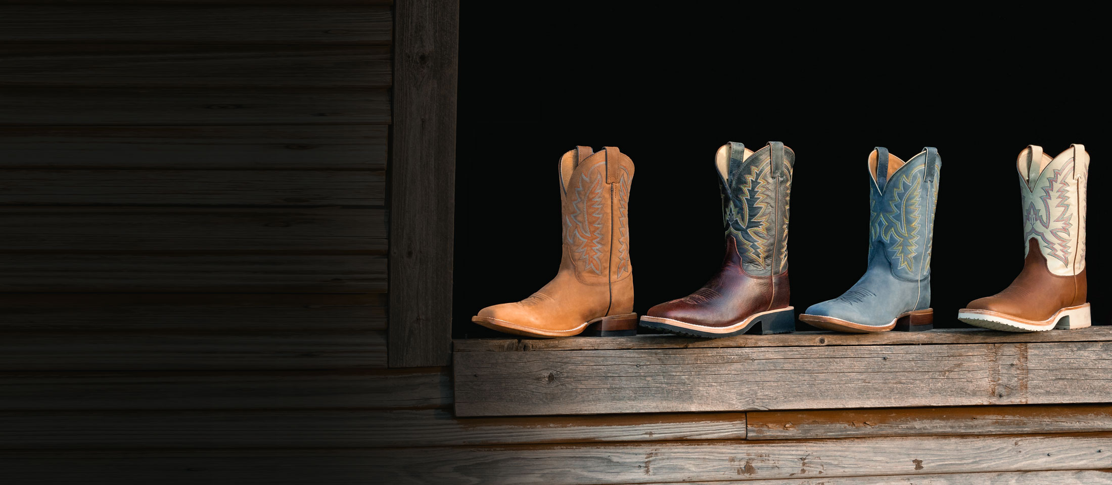 Men’s Rancho 11” Western boots in grey, Men’s Rancho 11” Western boots in brown, Trainor 11” Western boots in brown and Trainor 11” Western boots in dark brown sitting on a window sill made of wood.