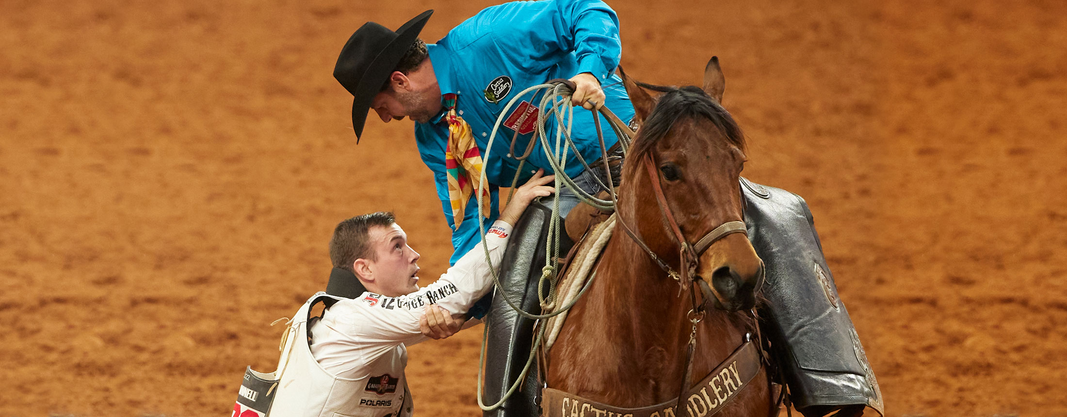 A pickup man is helping Tim O’Connell off his horse at the rodeo.