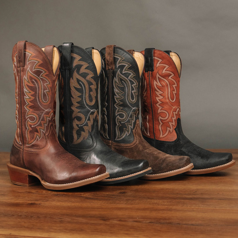 Men’s Cowboy Town Suede 13” Western boots in Chocolate and Onyx and Men’s Cowboy Town 13” Western boots in Bay and Midnight posed on a hardwood floor in front of a light grey wall.