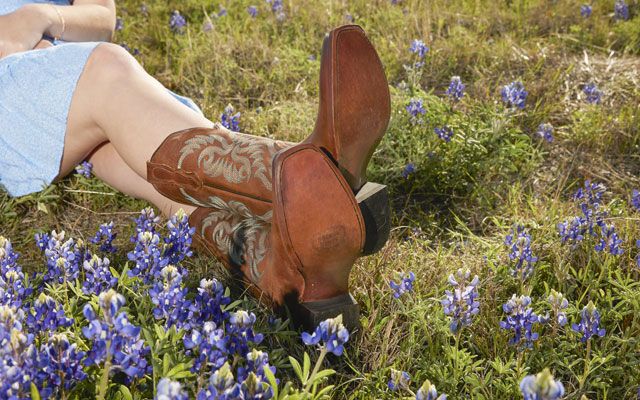 women sitting cross legged with brown boots on in a field of bluebonnets.