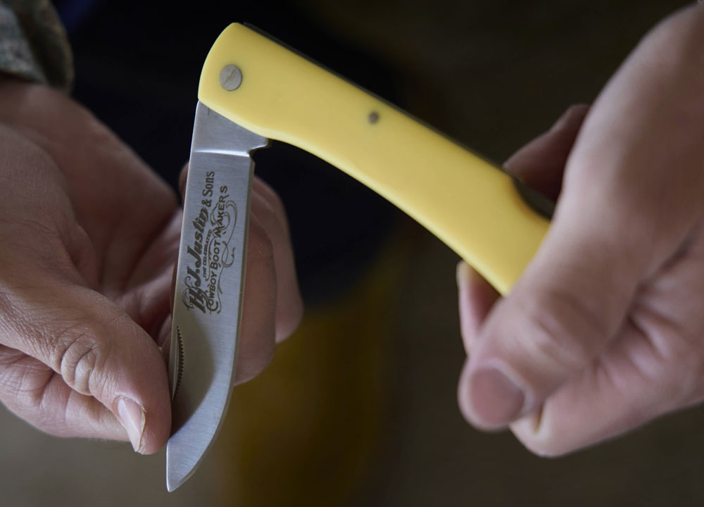 The Trapper Pocket Knife in yellow is being held open by a man, cleaning his fingernails. 