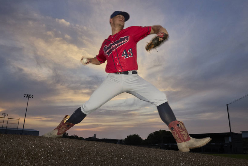 A baseball player wearing the men’s Pickett 11” Western in grey and red, throwing a baseball on a baseball field.