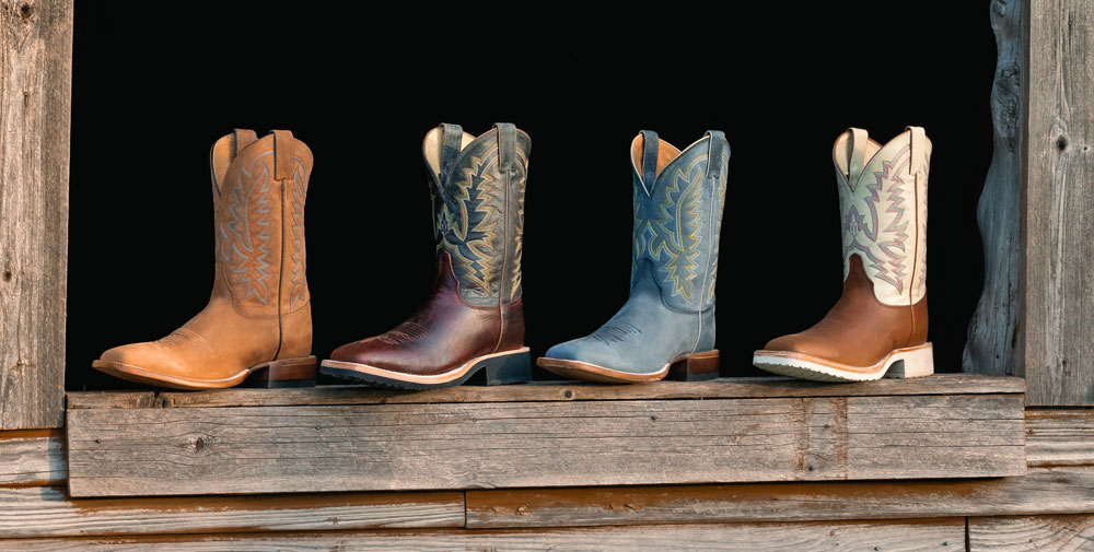 Men’s Rancho 11” Western boots in grey, Men’s Rancho 11” Western boots in brown, Trainor 11” Western boots in brown and Trainor 11” Western boots in dark brown sitting on a window sill made of wood.