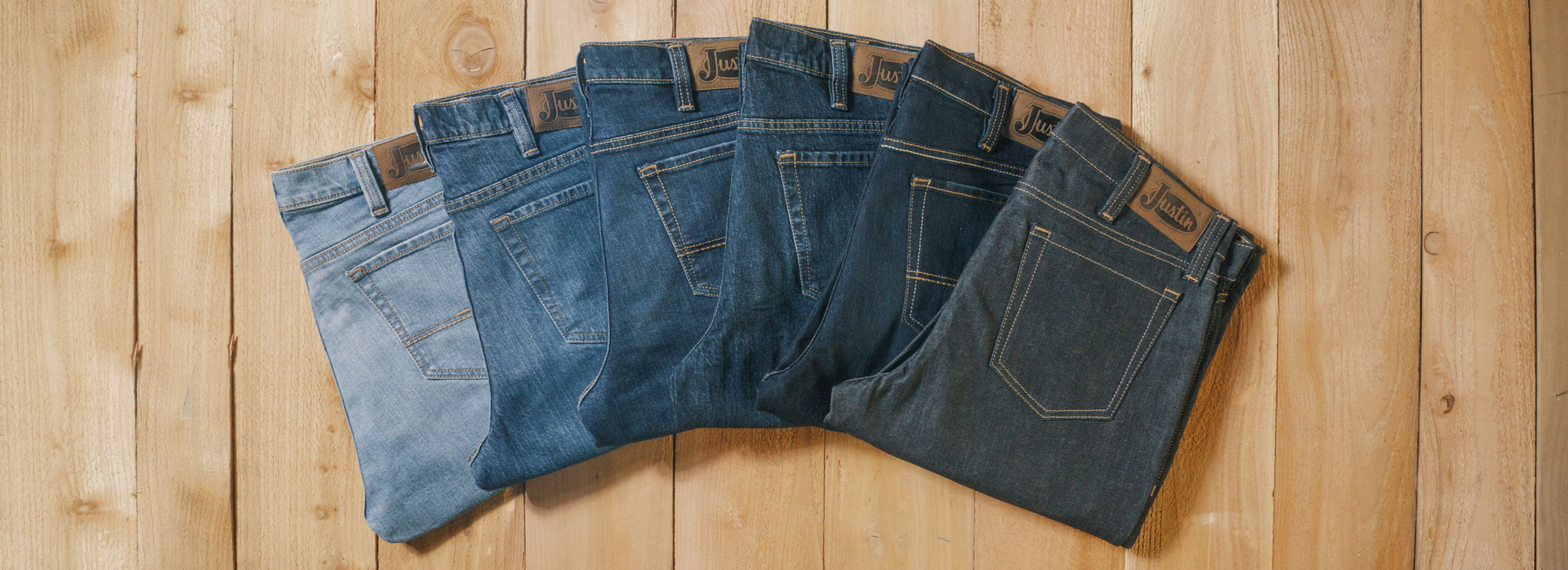 A fan of different washes of jeans ranging from light to dark denim laying on a wood background.