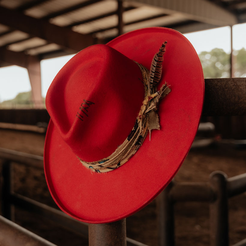 Women’s Joline Felt Western Hat in red leaning on a fence post at an arena. 