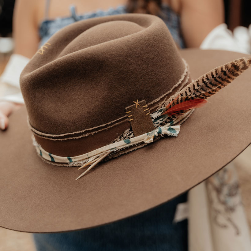 Hattie Felt Western Hat in brown with a feather being held.