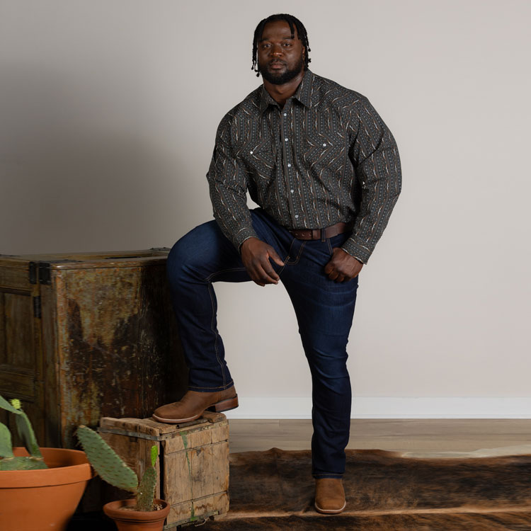 1879 Relaxed Bootcut Men's Jeans in dark wash blue worn by a man posing with his foot on a box. 
