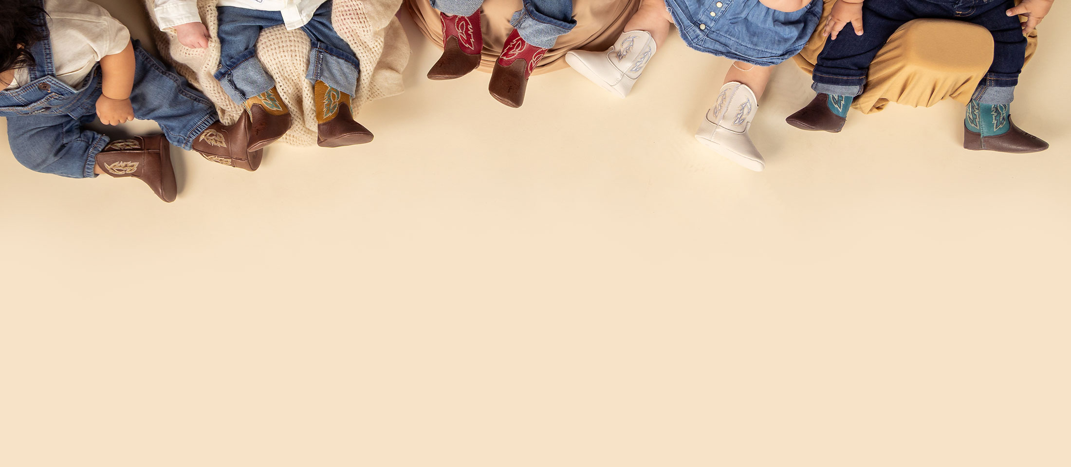 A group of infants wearing Justin Baby Canter in walnut (brown), Justin Baby Canter in pecan (tan), Justin Baby Canter in cognac (brown), Justin Bea in Arctic (white) an the Justin Baby Canter in cocoa (brown).