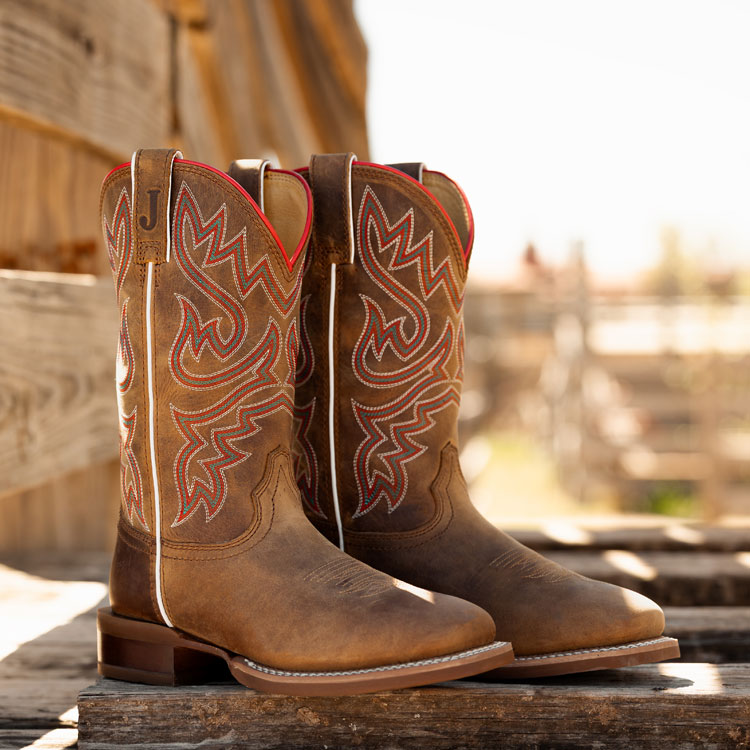 A pair of Little Sugar 11" cowgirl boots with red stitching sit on a wooden fence.