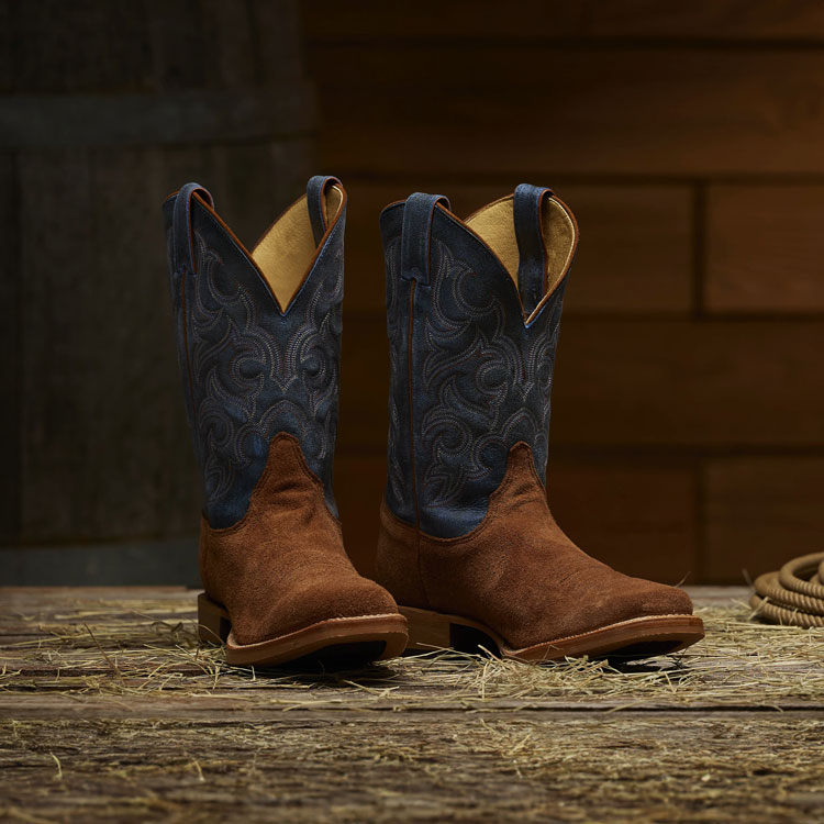 A pair of Fergus 11” cowboy boots sit on a wooden barn floor next to a coiled rope.