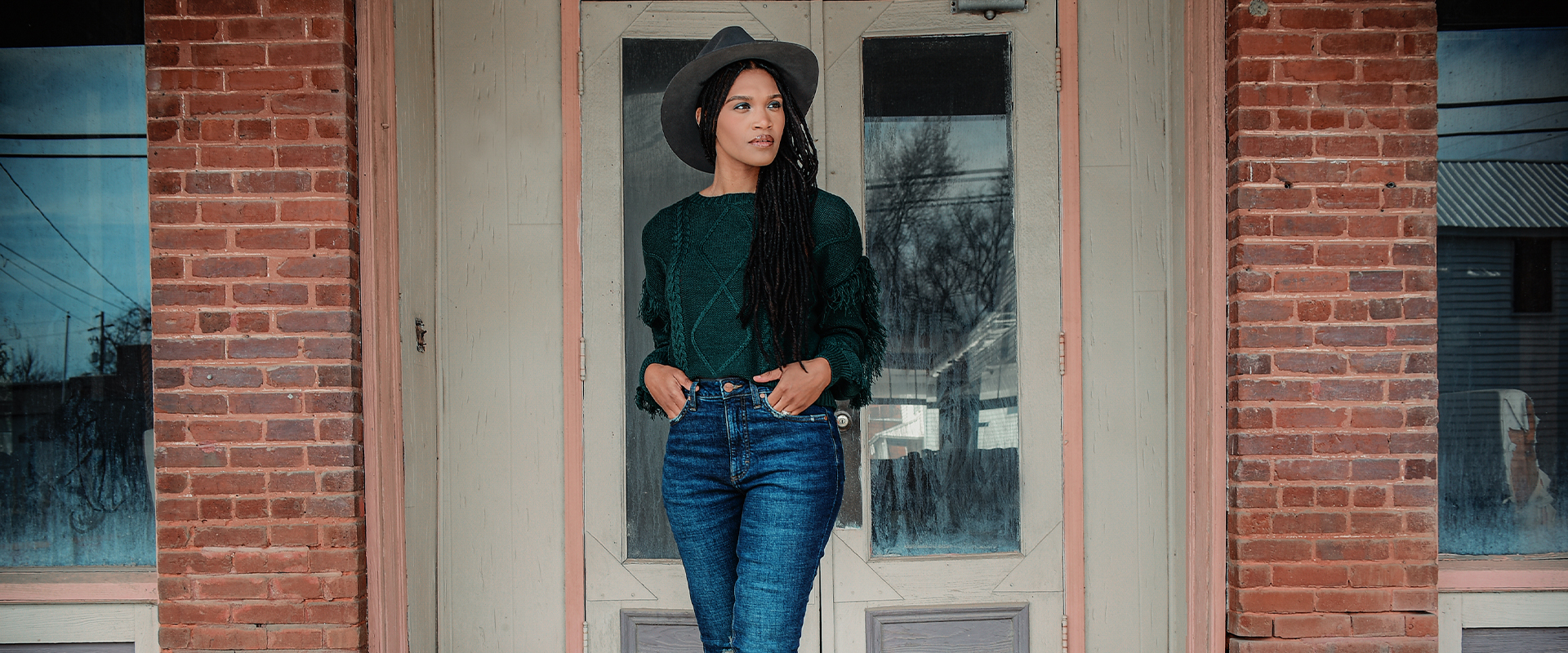 Cadance in doorway in black hat, green sweater and jeans