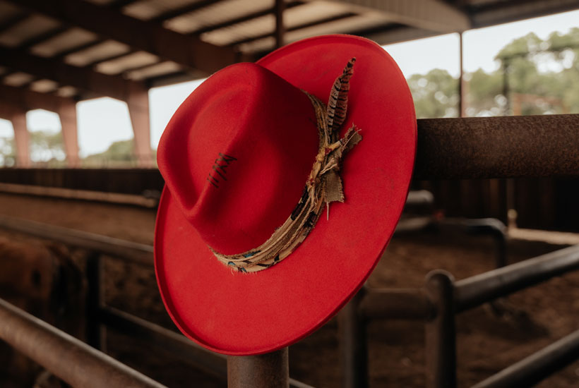 Women’s Joline Felt Western Hat in red leaning on a fence post at an arena. 