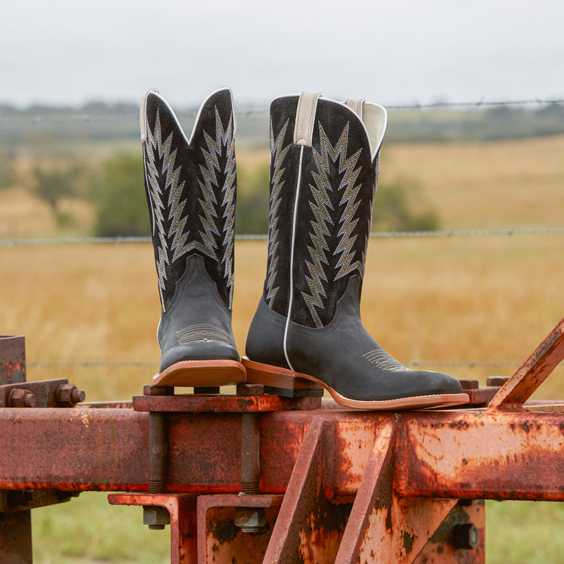 Men’s Hombre 13” suede Western boots in matte black posed on ranch equipment. 
