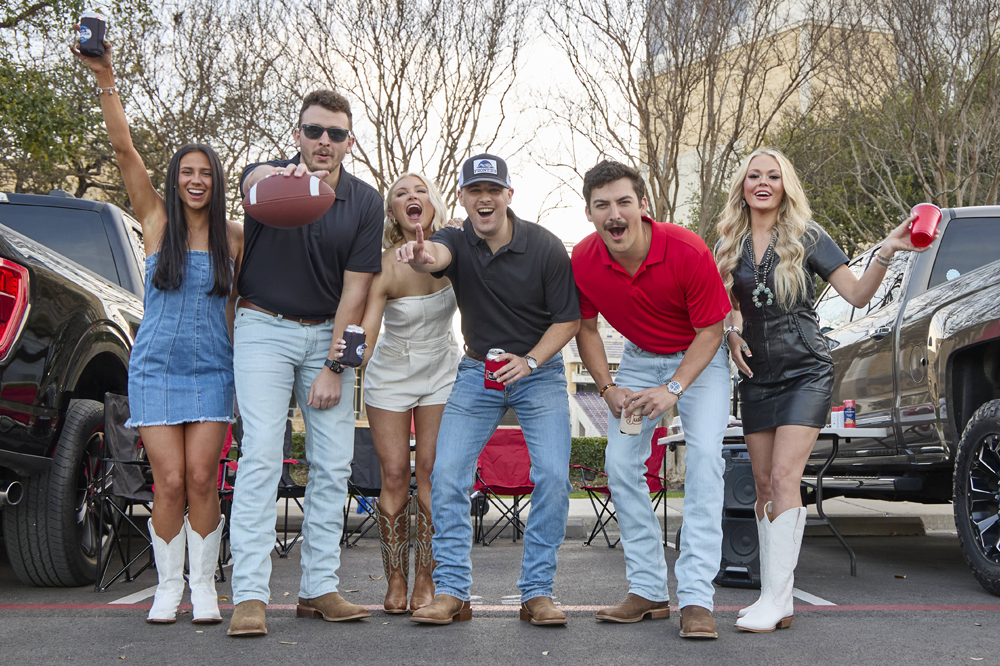 A group of young men and women tailgating between trucks, wearing Justin Boots.