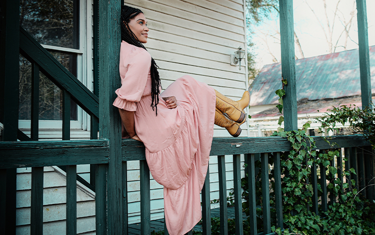 Cadance in pink dress and yellow boots sitting on banister outside house 