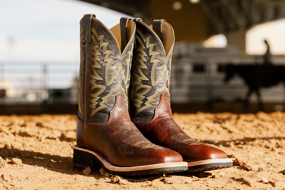 Men’s Trainor 11” Western boots in brown, sitting in dirt with the sun shining on the boots.