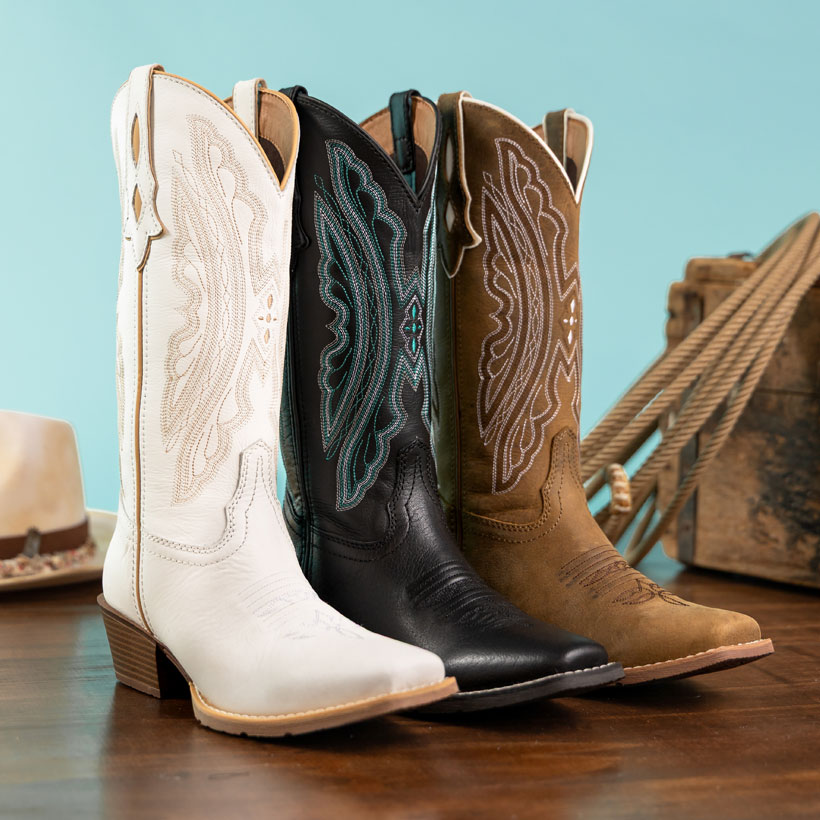 Rae 12” Western boots in brown, Rae 12” Western boots in  black, and Rae 12” Western boots in white, posed in front of a turquoise background and next to a western hat and a rope.