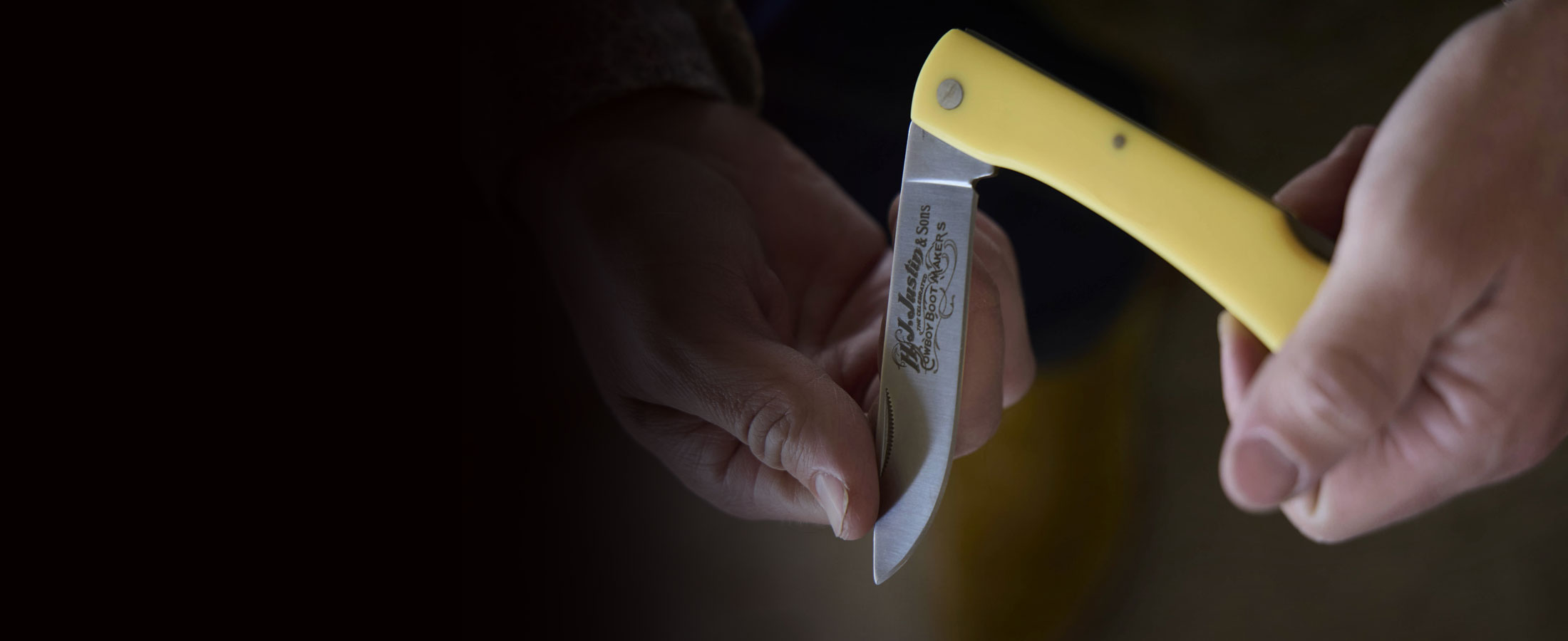 The Trapper Pocket Knife in yellow is being held open by a man, cleaning his fingernails. 