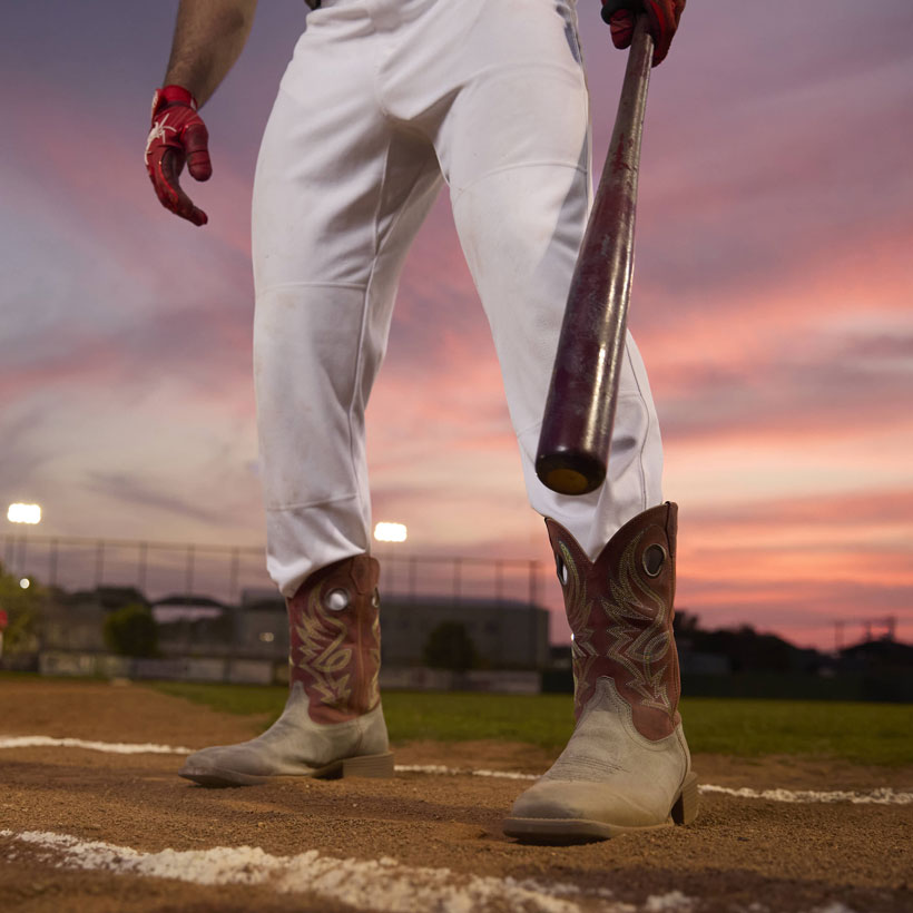 A man wearing the Men’s Pickett 11” Western boot in greige grey standing on a baseball field while holding a baseball bat