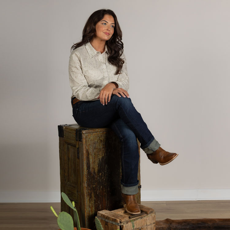 Rein 12” Western Boot in brown worn by a woman sitting on a box with her legs crossed.
