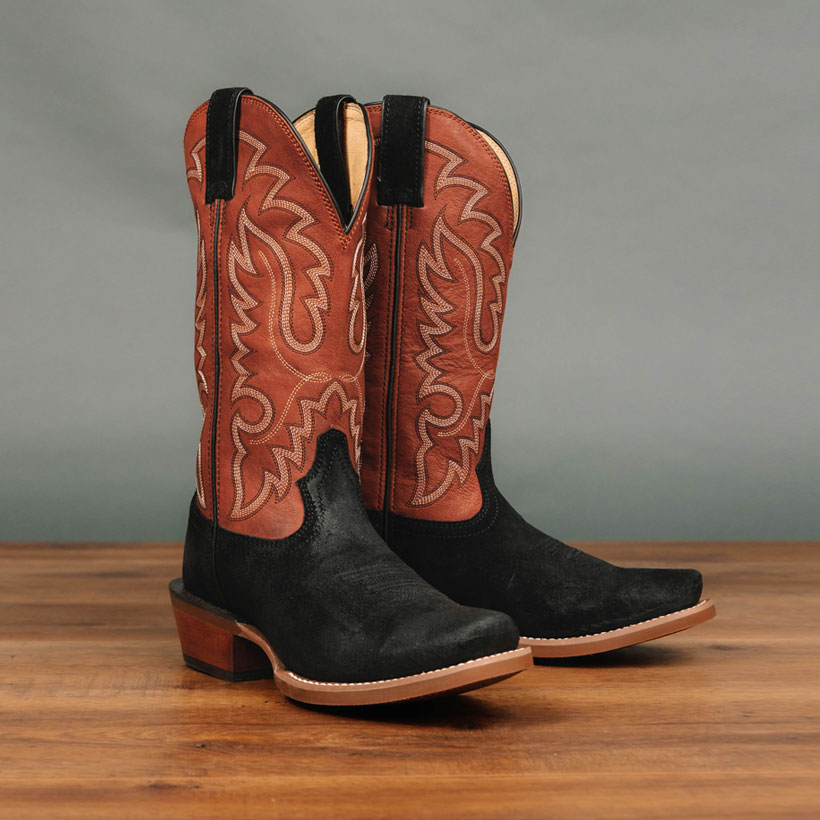 Men’s Cowboy Town Suede 13” Western boots in black and orange sitting on wood in front of a gray background.