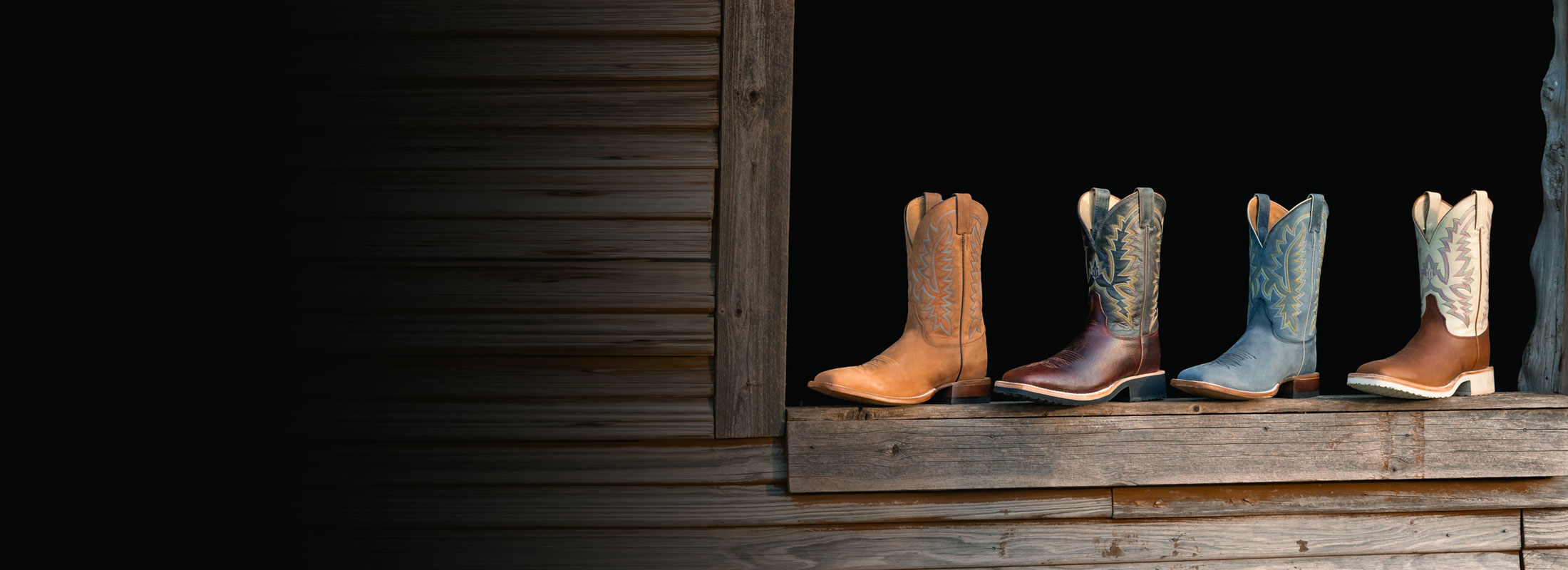 Men’s Rancho 11” Western boots in grey, Men’s Rancho 11” Western boots in brown, Trainor 11” Western boots in brown and Trainor 11” Western boots in dark brown sitting on a window sill made of wood.